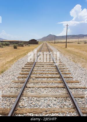 Bahn in der Wüste. Perspektivischer Blick mit blauem Himmel im Rücken. Landschaft in Utah USA. Eisenbahn mit Schroten Felsen und Eisenbahnstrümmer. Stockfoto