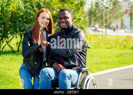 afro-amerikanischer Mann auf Rollstuhl sitzend, seine rothaarige Ingwer-Freundin Rolling Kinderwagen im Herbst Park. Mit romantischen Datum Stockfoto