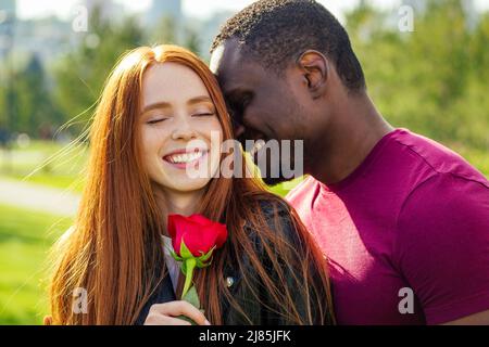 Nahaufnahme eines interracial Paares mit weißer Rose im Herbstpark im Frühjahr Stockfoto