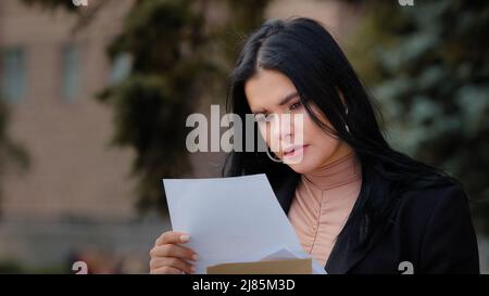 Nahaufnahme ernsthafte junge Frau im Freien sitzen Lesen Papier Brief traurig Mädchen fühlt sich Ärger über schlechte Nachrichten aufgeregt finden Sie heraus über gescheiterte Prüfungen Hochschule Stockfoto