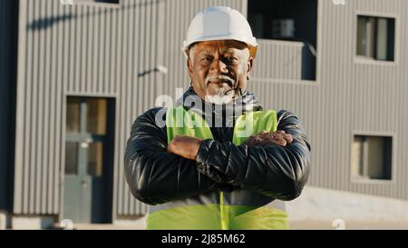 Nahaufnahme älterer afroamerikanischer Bauarbeiter, der in Schutzhelm-Uniform im Freien stand selbstbewusster Arbeiter kreuzte die Arme über die Brust Stockfoto