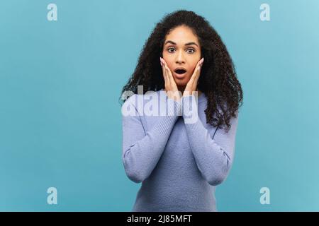 Nahaufnahme des Portraits einer überraschten multirassischen Dame. Verblüffte afroamerikanische Frau in violettem Pullover hält Küken und schaut mit offenem Mund isoliert auf blau auf die Kamera. Unglaubliche Promotion Stockfoto