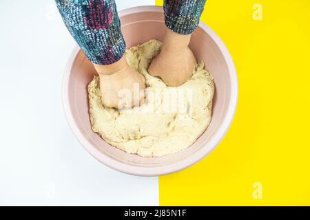 Kneten von Teig im Kunststoffkoffer, Brotkonzept, Draufsicht, isoliert auf weißem und gelbem Hintergrund, Kneten von Teig für Brot mit Kopierplatz Stockfoto