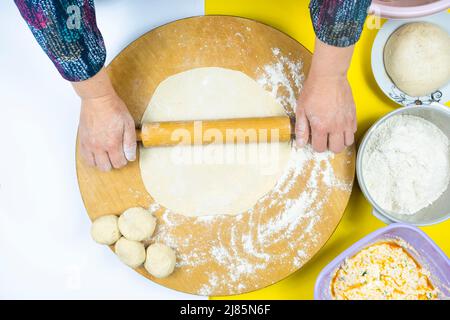 Frau rollt Gebäck auf traditionellen Kreis Holzbrett mit Zutaten, Draufsicht auf Walze, Teig und etwas Mehl, Kochkonzept, Zutaten Stockfoto