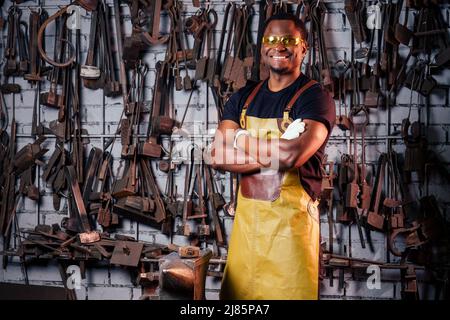 Hammerindustrie Small Business Concept.african american Mann in historischer Kleidung ist hämmern auf den Amboss gekleidet. Ein Schmied schmiedet ein Metall Stockfoto