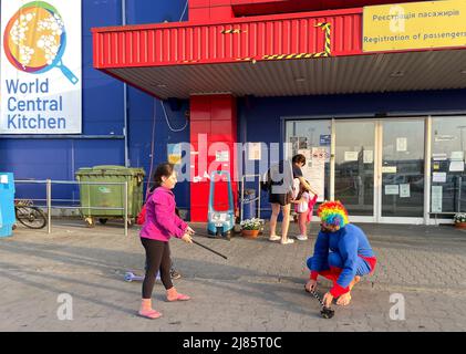 Przemysl, Polen:12. Mai 2022, Georgie mit Mobile Circus for Peace und Cabuwazi, Wanderzirkus für Kinder, spielt mit einem ukrainischen Mädchen und erfreut es. Er kam von Berlin nach Polen, um für die Flüchtlingskinder und -Erwachsenen im Tesco, einem ukrainischen Verarbeitungszentrum für humanitäre Hilfe in Przemysl, Polen, nahe der Grenze zu Medyka, aufzutreten und brachte Hunderte von traurigen Menschen, die gerade aus Charkiw, Kiew, in der einladenden polnischen Grenzstadt angekommen sind, zum Lachen. Odessa und andere Orte unter Beschlagnahme durch russische Invasoren. Hier spielen Kinder zusammen oder lächelnde Erwachsene sind ein sehr ungewöhnlicher Anblick: Stockfoto
