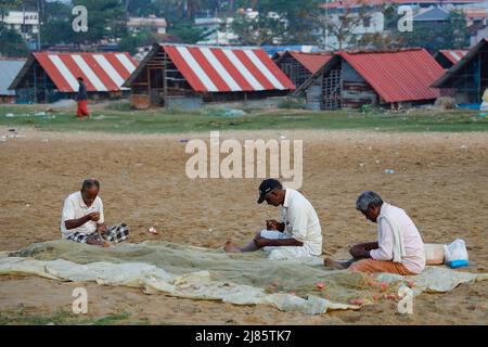 Drei Fischer, die am Strand sitzen und ihre Fischernetze ausbessern, Tangassery, Kerala, Indien. Stockfoto