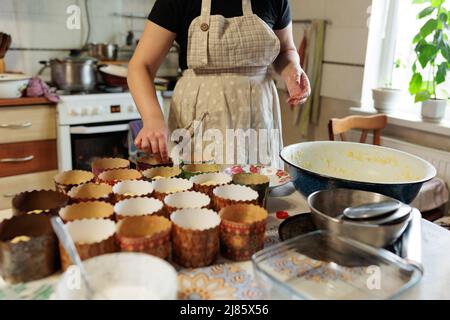 Eine Frau Köchin legt Teig mit kandierten Früchten in Papierformen zum Backen von Ostergebäck. Familientraditionen und Rezepte. Kleines Familienunternehmen und prepa Stockfoto
