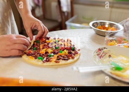 Weibliche Hände verdrehen den Teig mit Rosinen und kandierten Früchten. Roher Kuchenteig für Kraffin Stockfoto