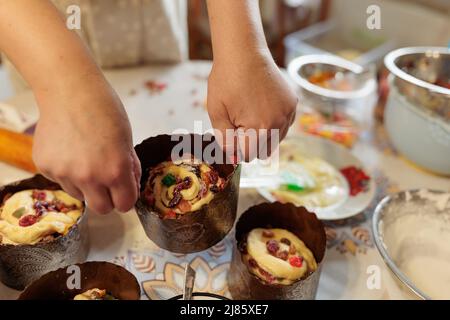 Eine Frau Köchin legt Teig mit kandierten Früchten in Papierformen zum Backen von Ostergebäck. Familientraditionen und Rezepte. Kleines Familienunternehmen und Stockfoto