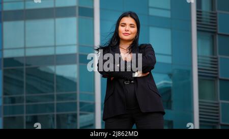 Junge hispanische Geschäftsfrau Angestelltenfirma, die selbstbewusst Arme im Freien auf Bürogebäude im Hintergrund stehend und die Kamera in posiert sieht Stockfoto