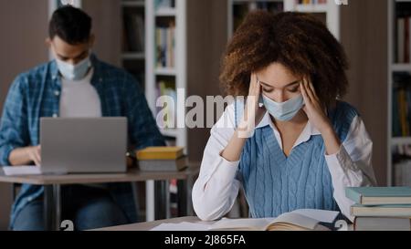 Zwei Studenten in Schutzmaske sitzen im Klassenzimmer in der Universitätsbibliothek tun Hausaufgaben Prüfungsvorbereitung junges Mädchen auf der Suche nach Informationen im Buch Stockfoto