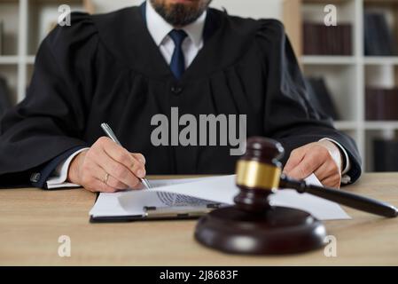 Dunkelbrauner Richter Gavel auf Schallblock auf dem Tisch vor dem Hintergrund der Richterunterzeichnung Urteil platziert. Stockfoto