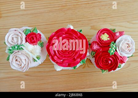 Draufsicht auf wunderschöne rosa Blumenstrauß geformte Zuckerguss Cupcakes Line-up auf Holz Hintergrund Stockfoto