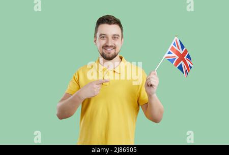 Glücklicher junger Mann, der Englisch lernt, hält die Flagge Großbritanniens und lächelt Stockfoto