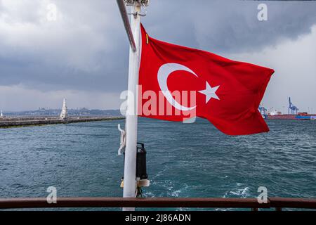 Eine rote türkische Flagge mit dem Halbmond und dem Stern wird auf der Rückseite einer Fähre gesehen. Der Seeverkehr mit Fähren ist eine Besonderheit Istanbuls. Trotz des tiefsten Tunnels der Welt unter dem Bosporus für die U-Bahn und der Einweihung der neuen 'Canakkale 1915 Bridge' im März 2022 fördern die Bevölkerung und der 2019 neu gewählte Bürgermeister von Istanbul den Seeverkehr, um den Straßenverkehr zu entlasten und die Emissionen von CO2 zu reduzieren. Stockfoto