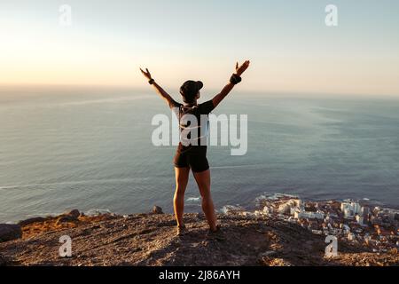 Rückansicht einer frauen Frau, die auf der Bergspitze steht, mit weit geöffneten Armen Stockfoto