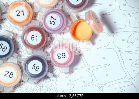 Offenes Glas mit Acrylfarbe auf Leinwand mit Markierungen Hintergrund. Malen nach Zahlen. Farbe nach Anzahl zu Hause Hobby. Nahaufnahme. Selektiver Fokus auf Gläser Stockfoto