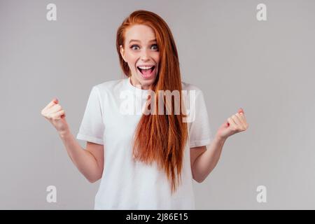 Rothaarige Ingwer Frau in weißer Baumwolle T-Shirt Daumen gekreuzt Wunsch das Beste in Studio grauen Hintergrund Stockfoto