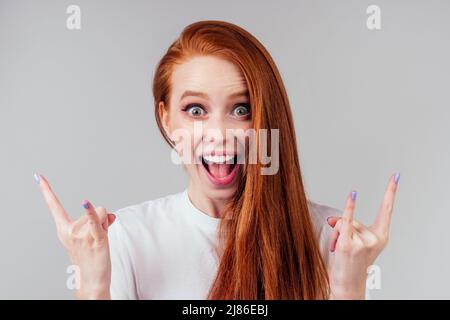 Rothaarige Ingwer-Frau in weißem Baumwoll-T-Shirt zeigt Felsen Finger Stockfoto