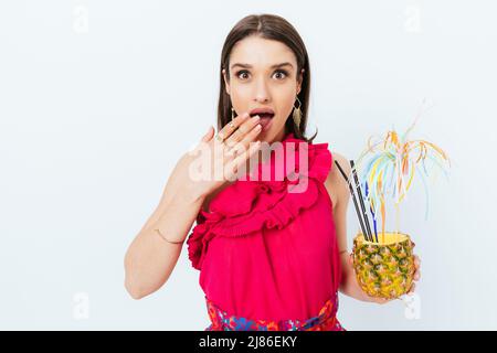 Entzückte stilvolle junge Frau hält festliche Ananas Cocktail auf weißem Hintergrund stehend Blick auf die Kamera überrascht Stockfoto