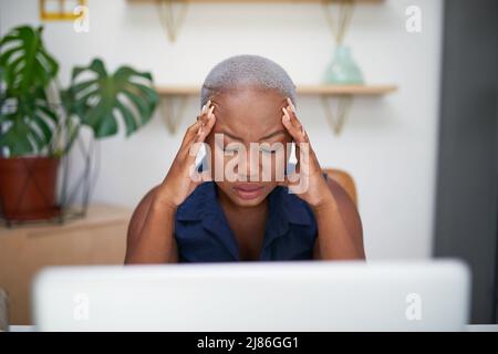 Eine gestresste junge schwarze Geschäftsfrau legt ihre Hände an ihren Kopf am Schreibtisch Stockfoto