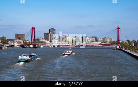 Rotterdam, Niederlande - 28. April 2022: Stadtbild von Rotterdam mit Booten auf dem Fluss Maas. Ein Blick auf den Willemsbrug, eine kabelgestaunte rote Brücke mit einem Stockfoto