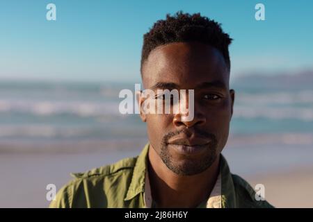 Nahaufnahme eines selbstbewussten, gutaussehenden afroamerikanischen jungen Mannes bei Sonnenuntergang gegen Meer und Himmel Stockfoto