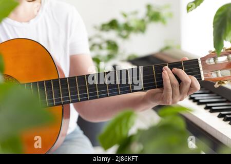 Frauenhände spielen die Gitarre. Finger kneifen die Saiten auf dem Griffbrett. Home-Musik machen, Entspannung. Biophile Inneneinrichtung. Viele Stockfoto