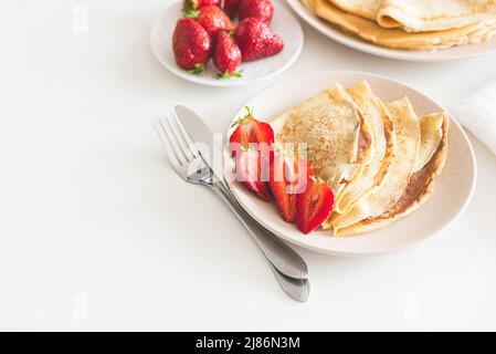 Französische Crepes mit Schokoladenaufstrich und Erdbeeren auf weißem Tisch Stockfoto