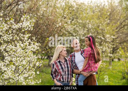 Glückliche Eltern, Mutter und Vater, Tochter, junge Familie im Frühling vor dem Hintergrund blühender Apfel- und Kirschbäume Stockfoto