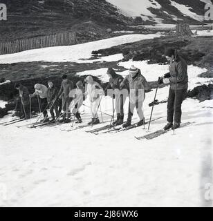 1960er, historisch, Highlands, Schottland, eine Gruppe von Skifahrern in der Winterkleidung der Epoche, mit einem Skiunterricht. Stockfoto