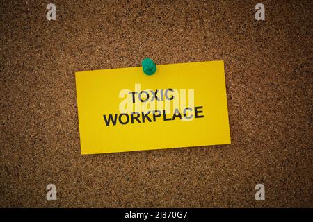Eine Haftnotiz mit den Worten Toxic Workplace darauf an einem Korkbrett befestigt. Nahaufnahme. Stockfoto
