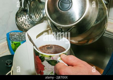 Eine Frau gießt heißes Wasser aus einem Wasserkocher in eine Tasse Kaffee. Stockfoto