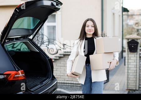 Junge Geschäftsfrau, die Pakete von einem Kofferraum abholt und mit dem Auto nach Hause kommt Stockfoto