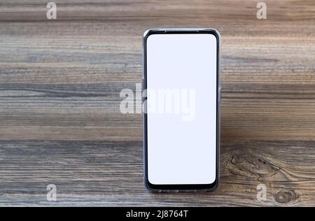 Smartphone mit weißem leeren Bildschirm, der auf einer Holzoberfläche mit Kopierfläche steht, Stockfoto