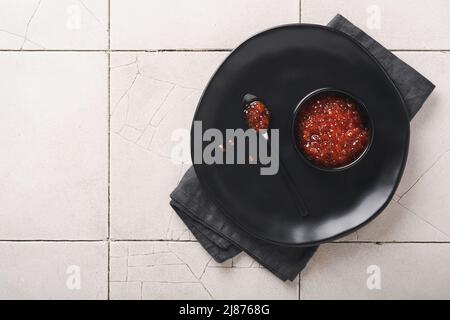 Kaviar mit rotem Lachs. Köstlicher roter Kaviar in schwarzer Schale auf altem rissigem Fliesenhintergrund. Draufsicht mit Kopierbereich. Flach liegend. Modell. Stockfoto