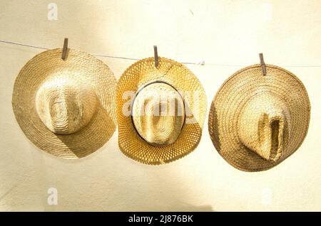 Drei Strohhüte hängen nach dem Waschen an einer Wäscheleine. Diese Arten von Hüten werden von Landwirten in ihren täglichen Routinen verwendet. Stockfoto