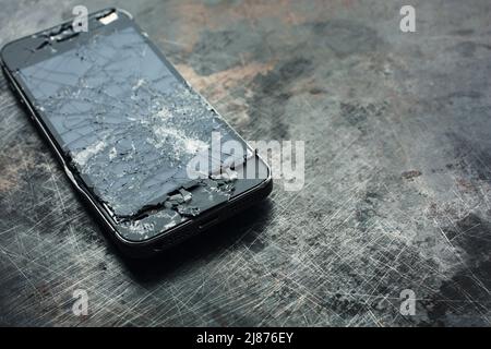 Stark beschädigtes Smartphone mit gebogenem Metallgehäuse und gebrochenem Glas auf grunge Hintergrund. Nahaufnahme. Stockfoto