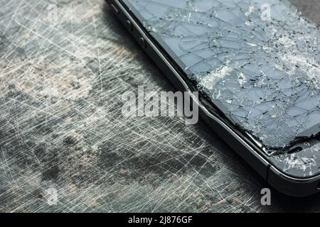 Stark beschädigtes Smartphone mit gebogenem Metallgehäuse und gebrochenem Glas auf grunge Hintergrund. Nahaufnahme. Stockfoto