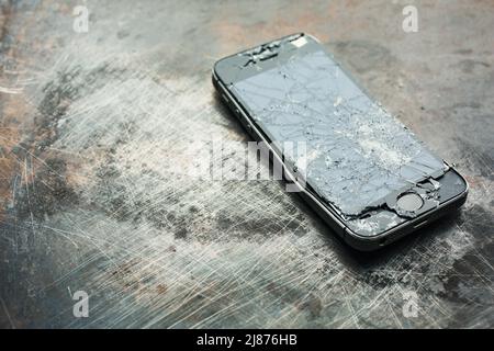 Stark beschädigtes Smartphone mit gebogenem Metallgehäuse und gebrochenem Glas auf grunge Hintergrund. Nahaufnahme. Stockfoto