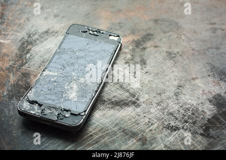 Stark beschädigtes Smartphone mit gebogenem Metallgehäuse und gebrochenem Glas auf grunge Hintergrund. Nahaufnahme. Stockfoto