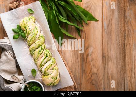 Geflochtenes Bärlauch-Pesto Brioche. Hausgemachtes rohes oder rohes frisches Pull-Apart-Brot mit Bärlauch-Pesto auf Holzbrett auf Holzhintergrundtisch. Stockfoto