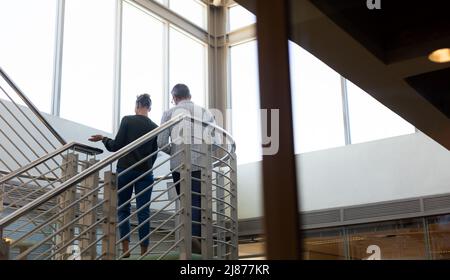 Aus der Perspektive der kaukasischen Kollegen, die diskutieren, während sie sich auf der Treppe am modernen Arbeitsplatz aufmachen Stockfoto