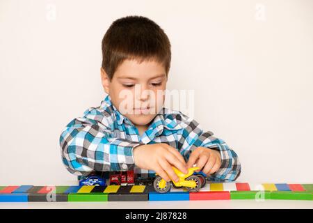 Vorschuljunge 4 Jahre alt spielt mit Autos und Spielzeug, Spiele für Kinder, Spielzeugladen auf weißem Hintergrund. Stockfoto