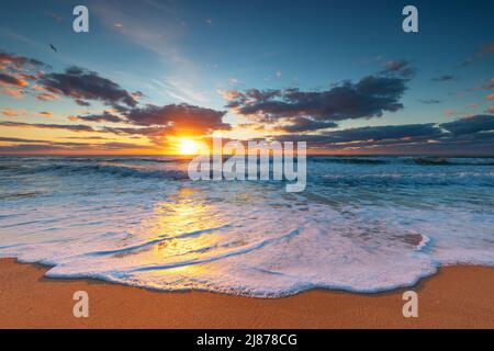 Wunderschöne Wolkenlandschaft über den Meereswellen und dem Strand, Sonnenaufgang Stockfoto