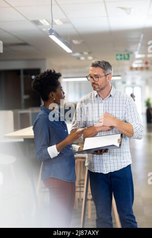 Junge afroamerikanische Geschäftsfrau diskutiert über Akte mit kaukasischem Geschäftsmann am Arbeitsplatz Stockfoto