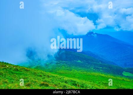 Das saftig grüne Tal vom Gipfel des Berges Hoverla aus gesehen gegen den bewölkten Himmel und die blauen Karpaten im Dunst, Ukraine Stockfoto