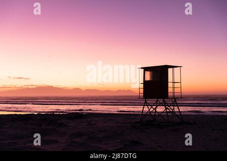 Blick auf Silhouette Rettungsschwimmerhütte am Sandstrand gegen Meer und purpurnen Himmel, Kopierraum Stockfoto