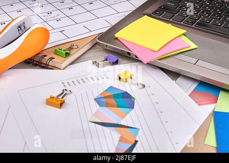 Arbeitspapiere mit Diagrammen und Binderclips. Haftnotizen mit Lapto und Hefter. Stockfoto